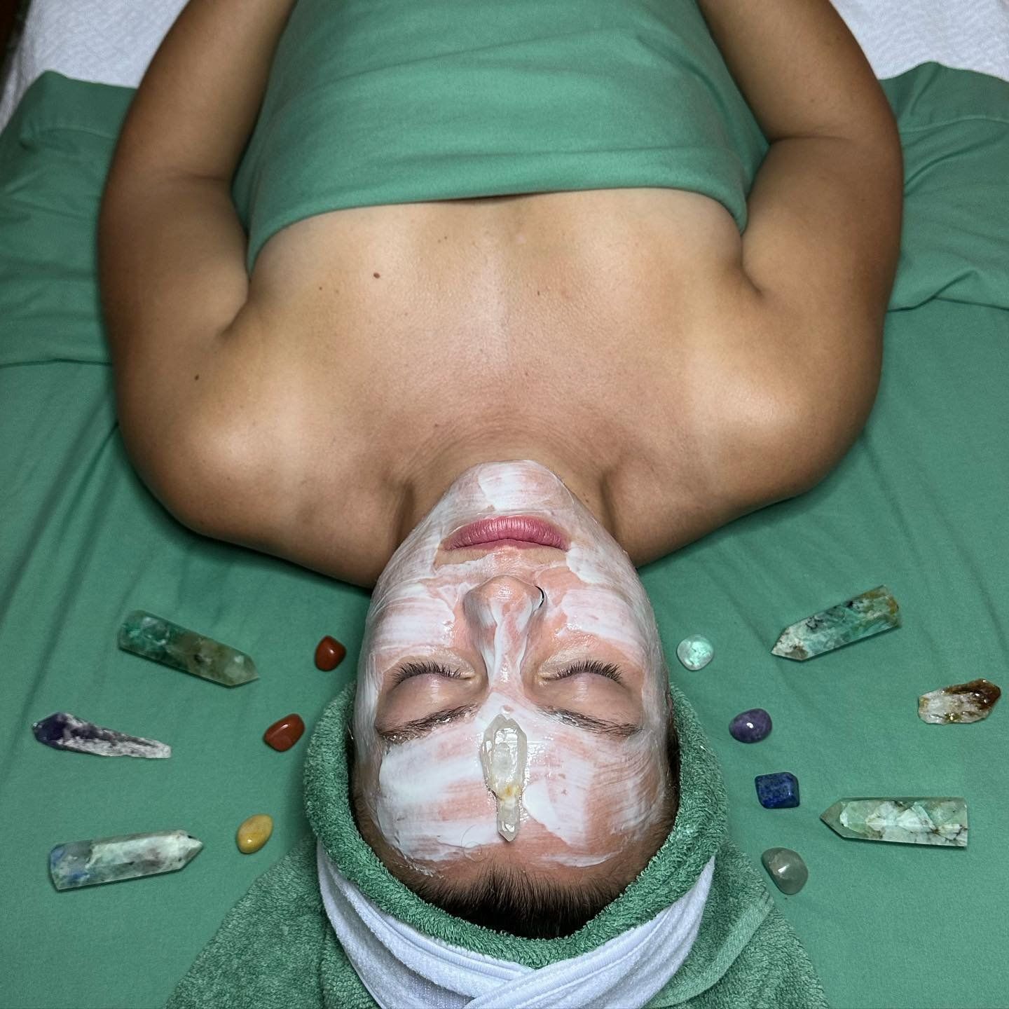 A woman is laying on a bed with a face mask and crystals around her