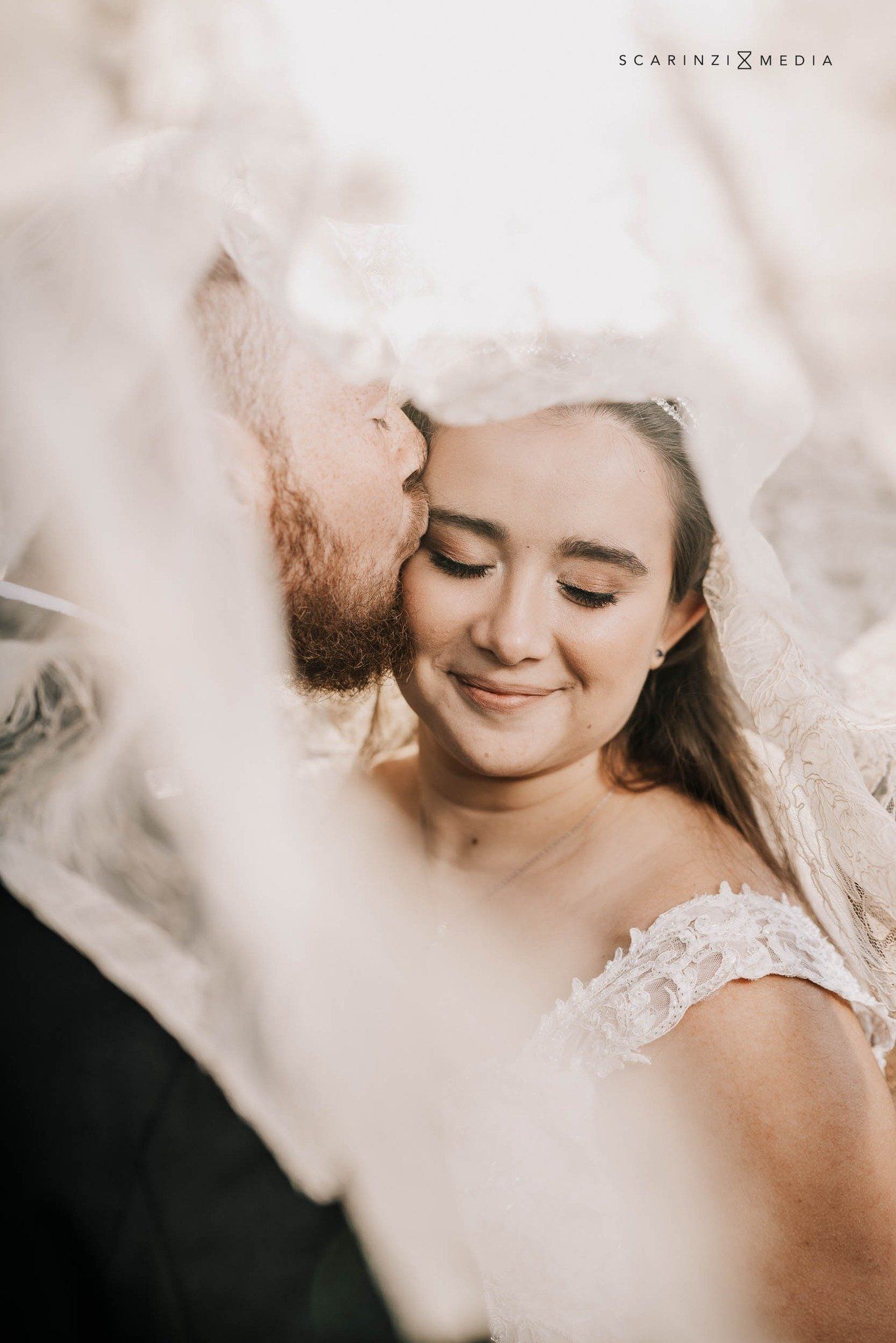 A bride and groom are kissing under a veil.