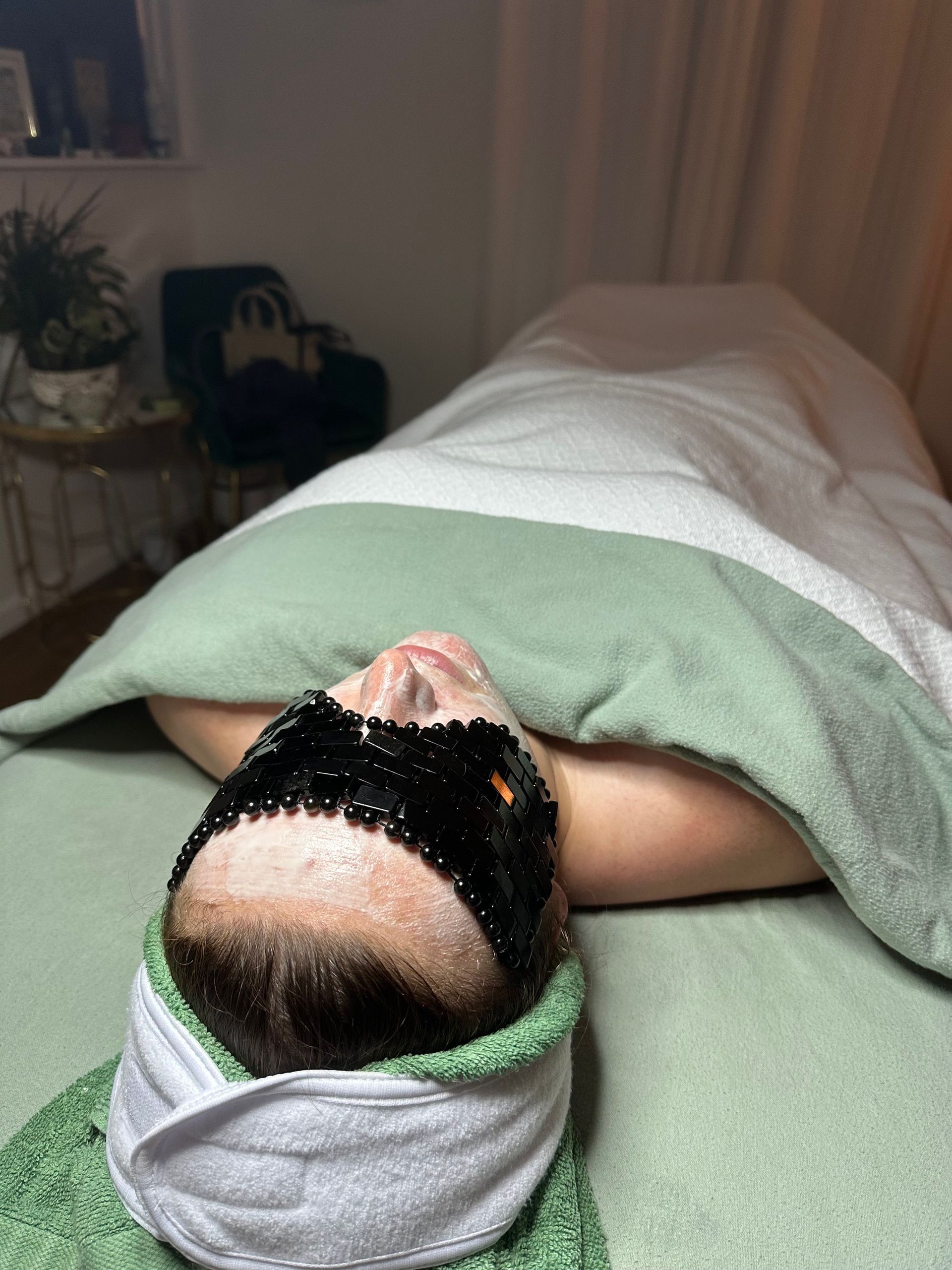 A woman is laying on a bed with a black mask on her face.