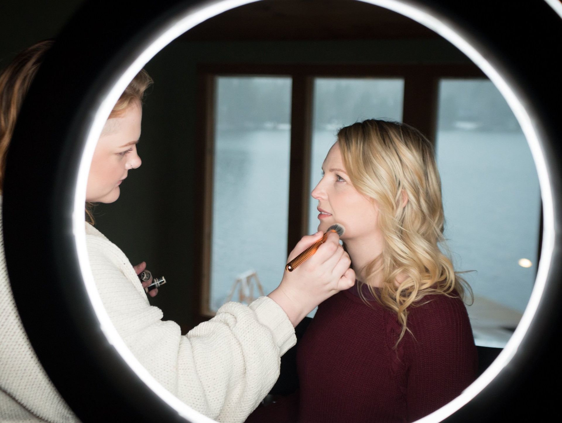 A woman is getting her makeup done in front of a mirror.