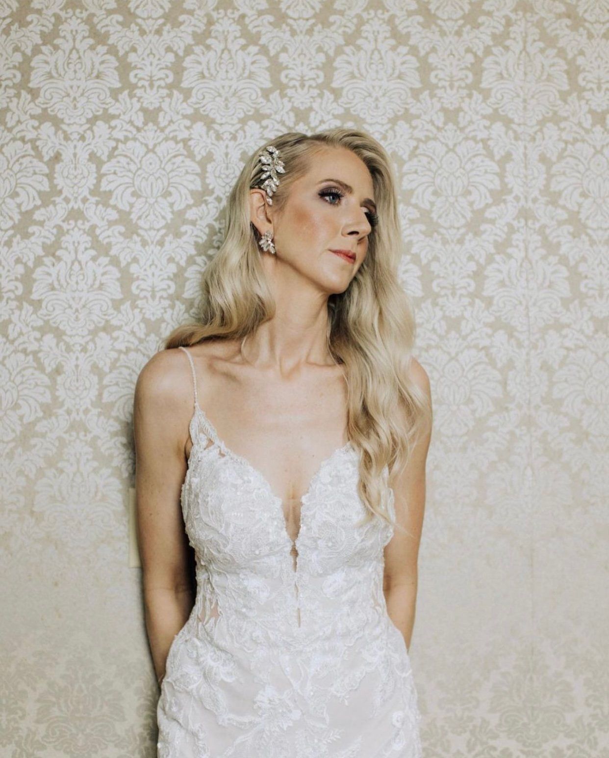 A woman in a wedding dress is standing in front of a wall.