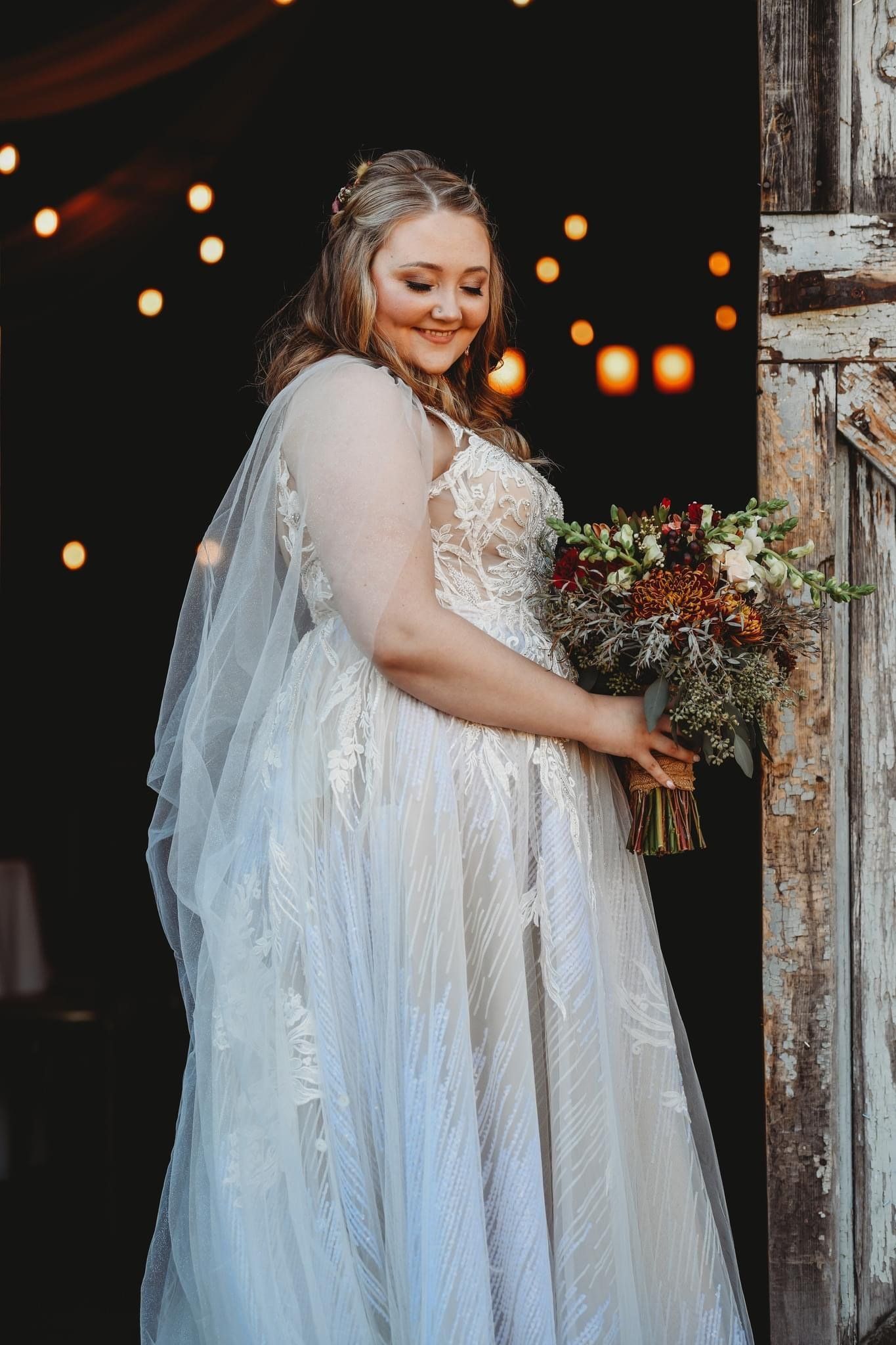 A bride in a wedding dress is standing in front of a door holding a bouquet of flowers.