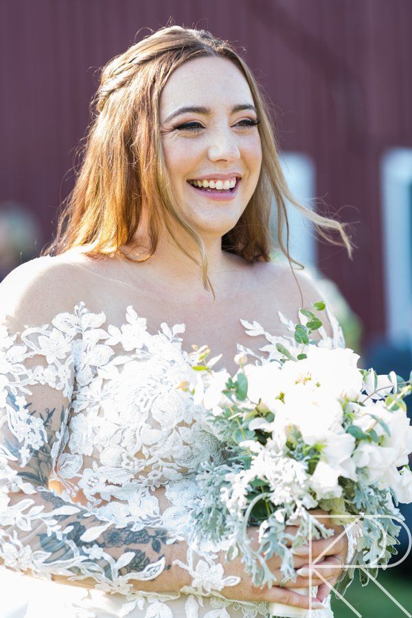 A bride in a white dress is holding a bouquet of white flowers and smiling.
