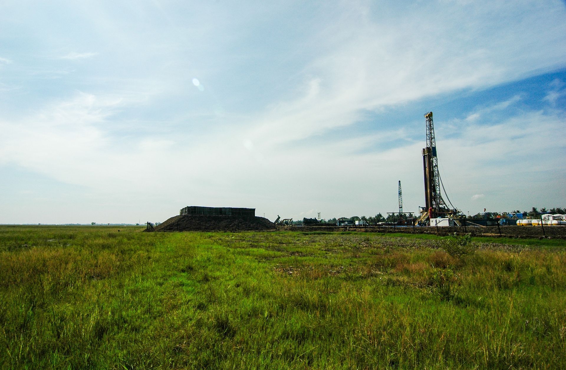 Drilling rig in a grassy field under a cloudy blue sky
