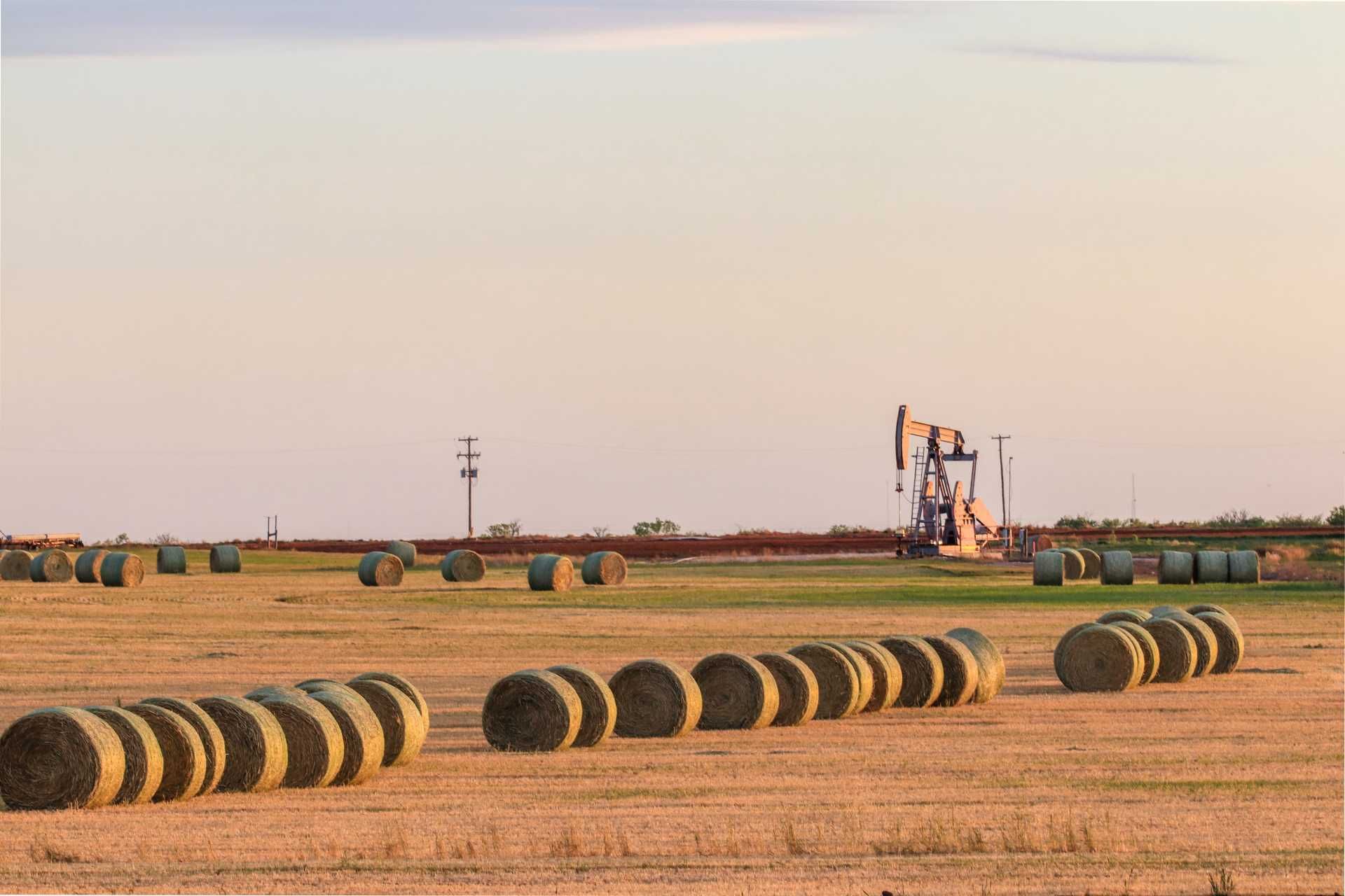 Hay bales in a field, oil pump jack in the distance under a dusky sky