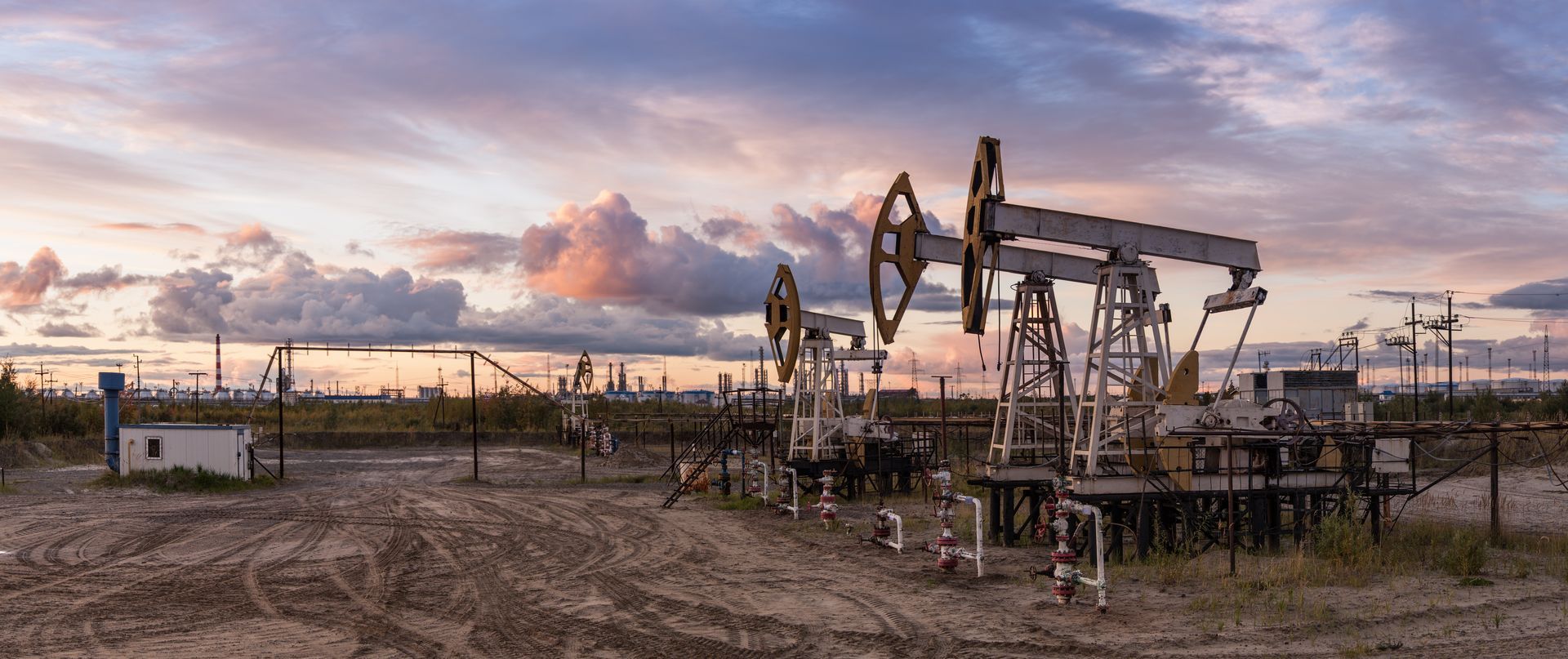 Oil pump jacks on a field, under a cloudy sunset sky