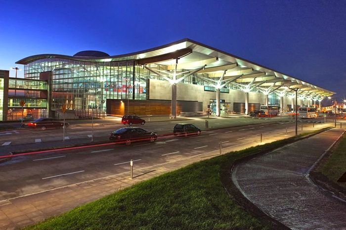 Modern glass-fronted airport terminal at dusk with cars and lit interior