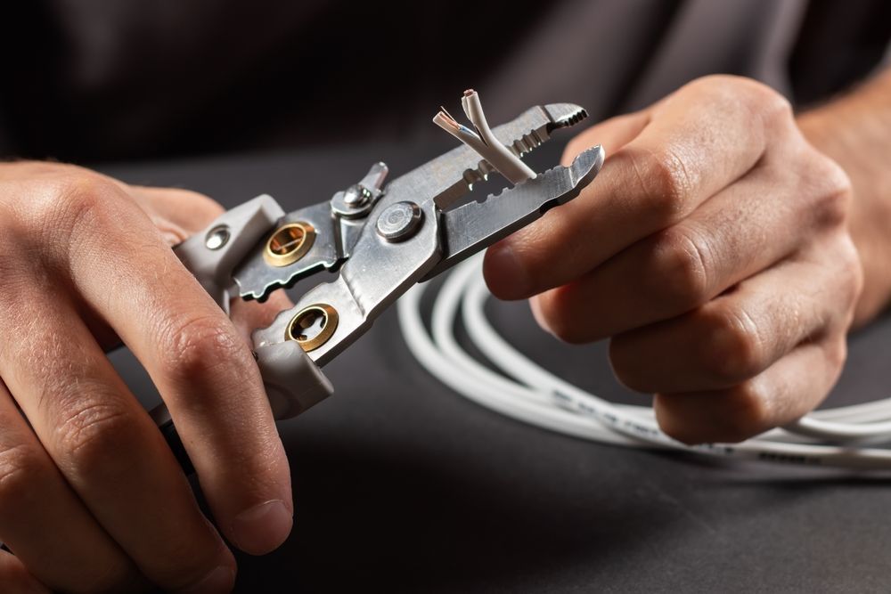Hands Using Wire Strippers to Cut and Strip White Electrical Wire — FAW Electrical in Kangaroo Valley, NSW
