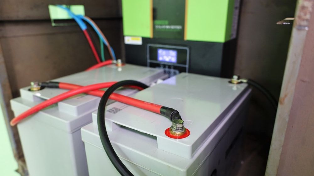 Two Connected Batteries With Red and Black Cables, in a Cabinet With a Green Inverter — FAW Electrical in Sussex Inlet, NSW