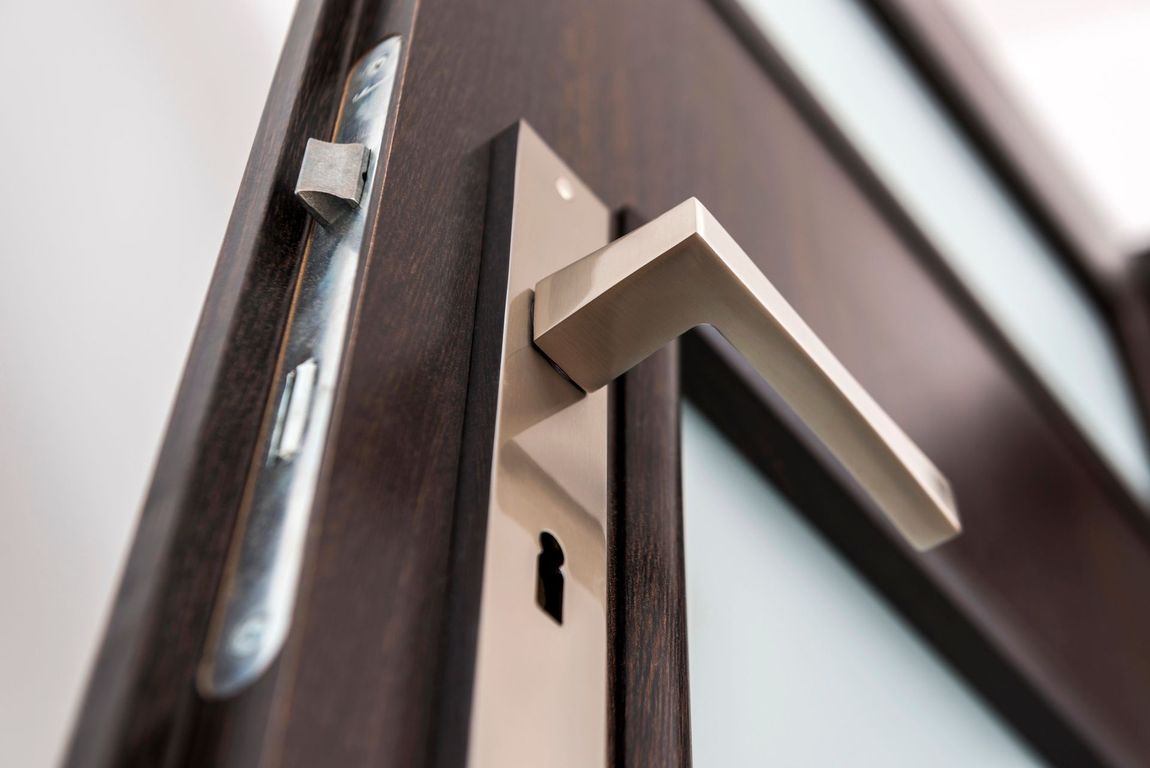 Primo piano di una maniglia argentata su una porta di legno scuro con serratura.