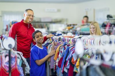 Father and son smiling while looking at clothes at a thrift store.
