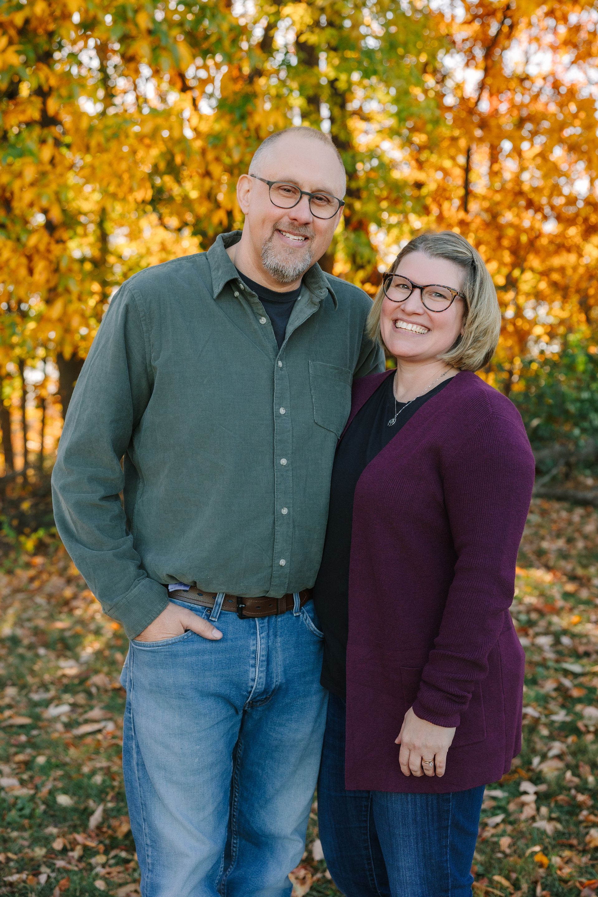 Couple smiling, outdoors in fall. Man wears green shirt, blue jeans; woman wears purple sweater, glasses. | SafeCar Auto Repair of Lancaster