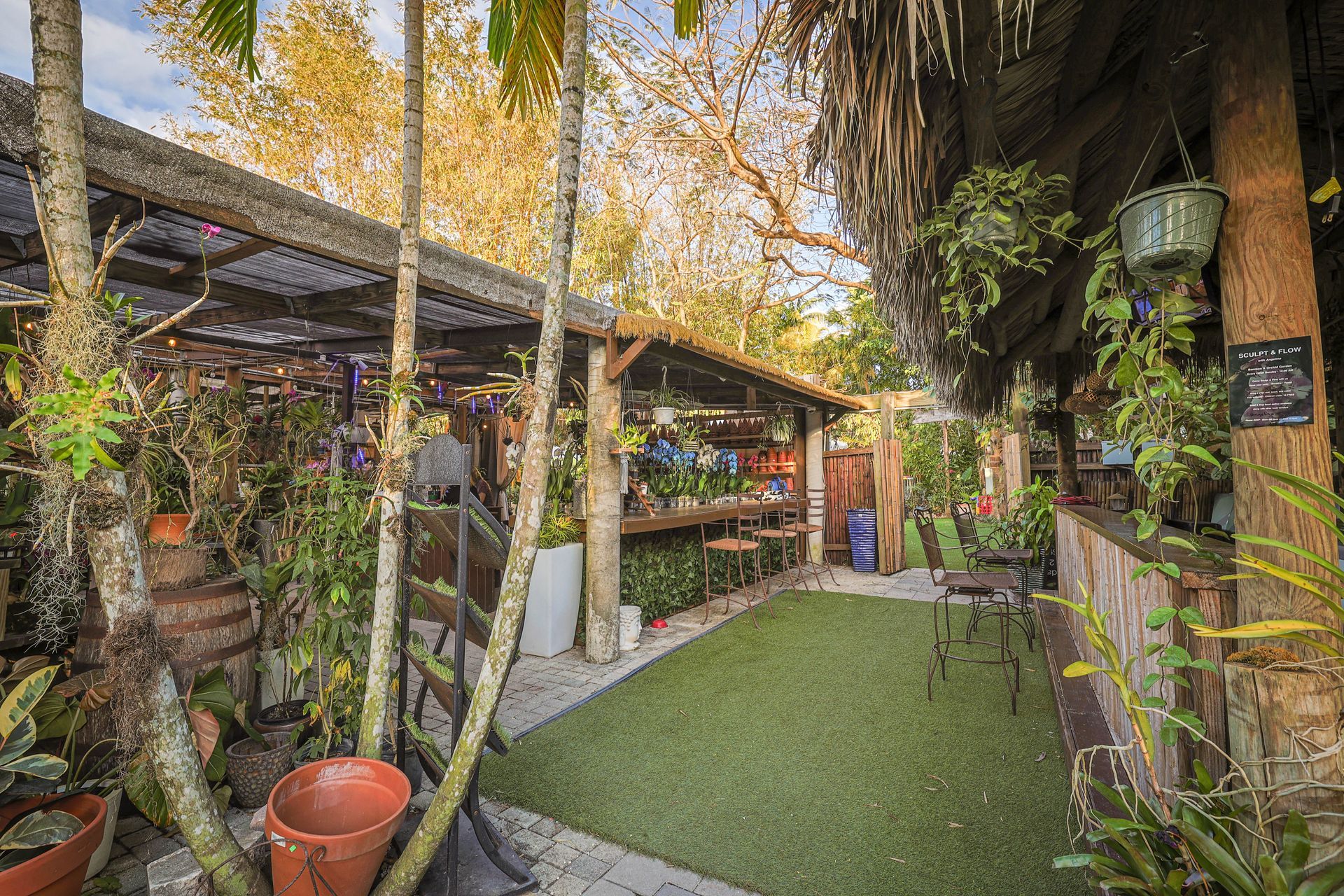 An outdoor, lushly landscaped bar area with a covered patio, artificial turf flooring, and rustic wooden accents.