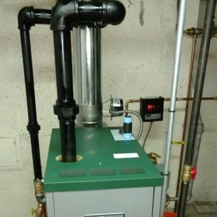 A green and gray residential furnace with black exhaust pipes in a basement.
