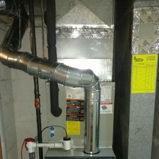 Furnace with metal ductwork, pipes, and labels in a basement setting.