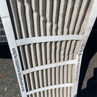 Dirty, used pleated air filter, with layers of collected dust and debris.