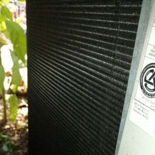 Close-up of a dark, pleated air conditioning condenser coil with a silver metal panel.