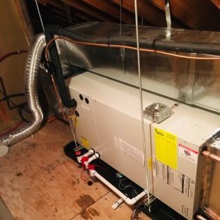 HVAC unit in attic, silver ductwork, white unit, copper piping.