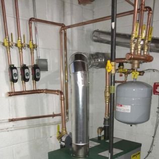 Copper piping and a boiler system in a utility room with a silver exhaust pipe and an expansion tank.