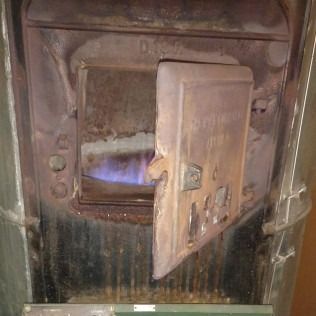 Rusty metal furnace door ajar, revealing a blue flame inside.