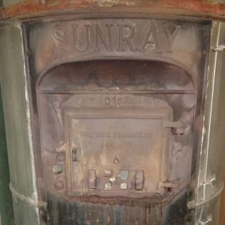 Sunray brand vintage stove, weathered metal exterior, central door, embossed brand name.