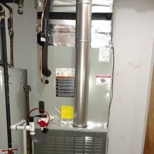 Furnace and water heater in a basement. Metal chimney, pipes, and control devices are visible.
