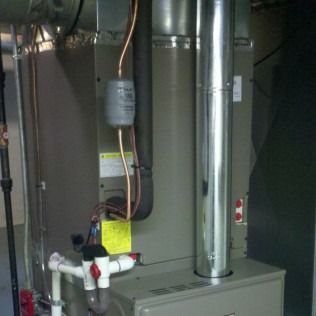 Furnace in a utility room with pipes, tubing, and vent stack. Gray and silver tones dominate.