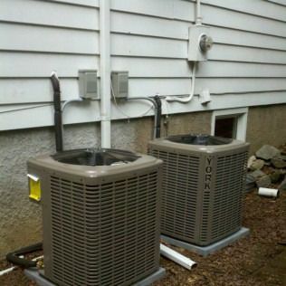 Two York air conditioning units outside a house, with electrical boxes and piping.