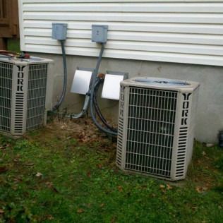 Two York air conditioning units outside a house with electrical connections in the side.