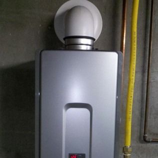 A tankless water heater mounted on a gray wall with exhaust vent and yellow gas line.