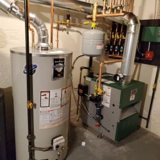 Water heater and boiler system with copper pipes and metal chimneys in a utility room.