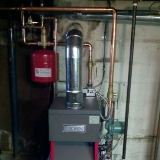 A Crown boiler with copper pipes, a red expansion tank, and a metal chimney in a basement setting.