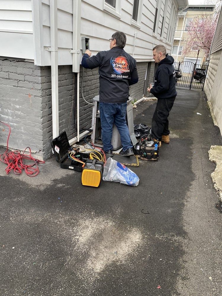 Two workers repairing equipment near a house. Tools and parts are on the ground.