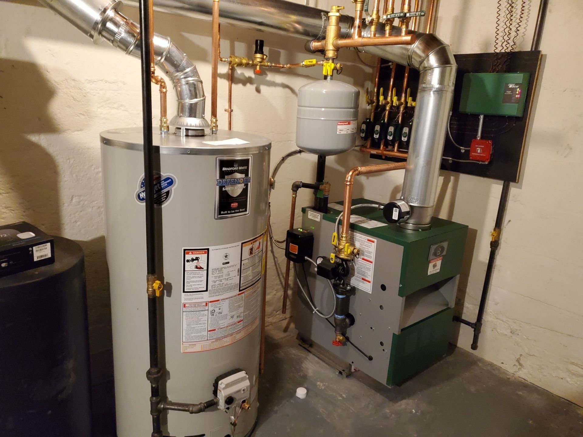 Water heater and furnace in a basement setting, with copper pipes and a metal expansion tank.