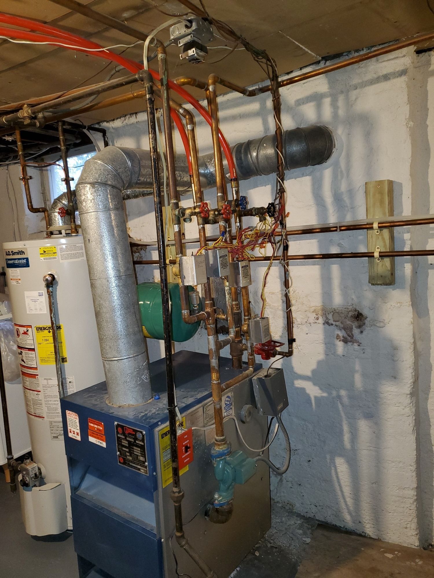 Heating system in a basement with water heater and copper piping. Blue furnace and silver ductwork are visible.