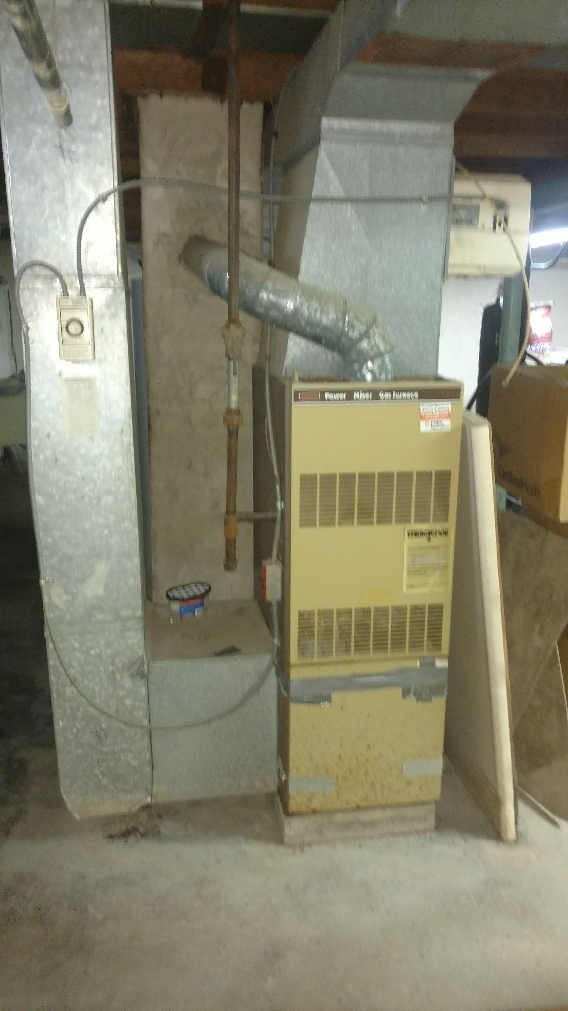 Furnace and ductwork in a basement setting. The furnace is tan, with silver ductwork and a concrete foundation.