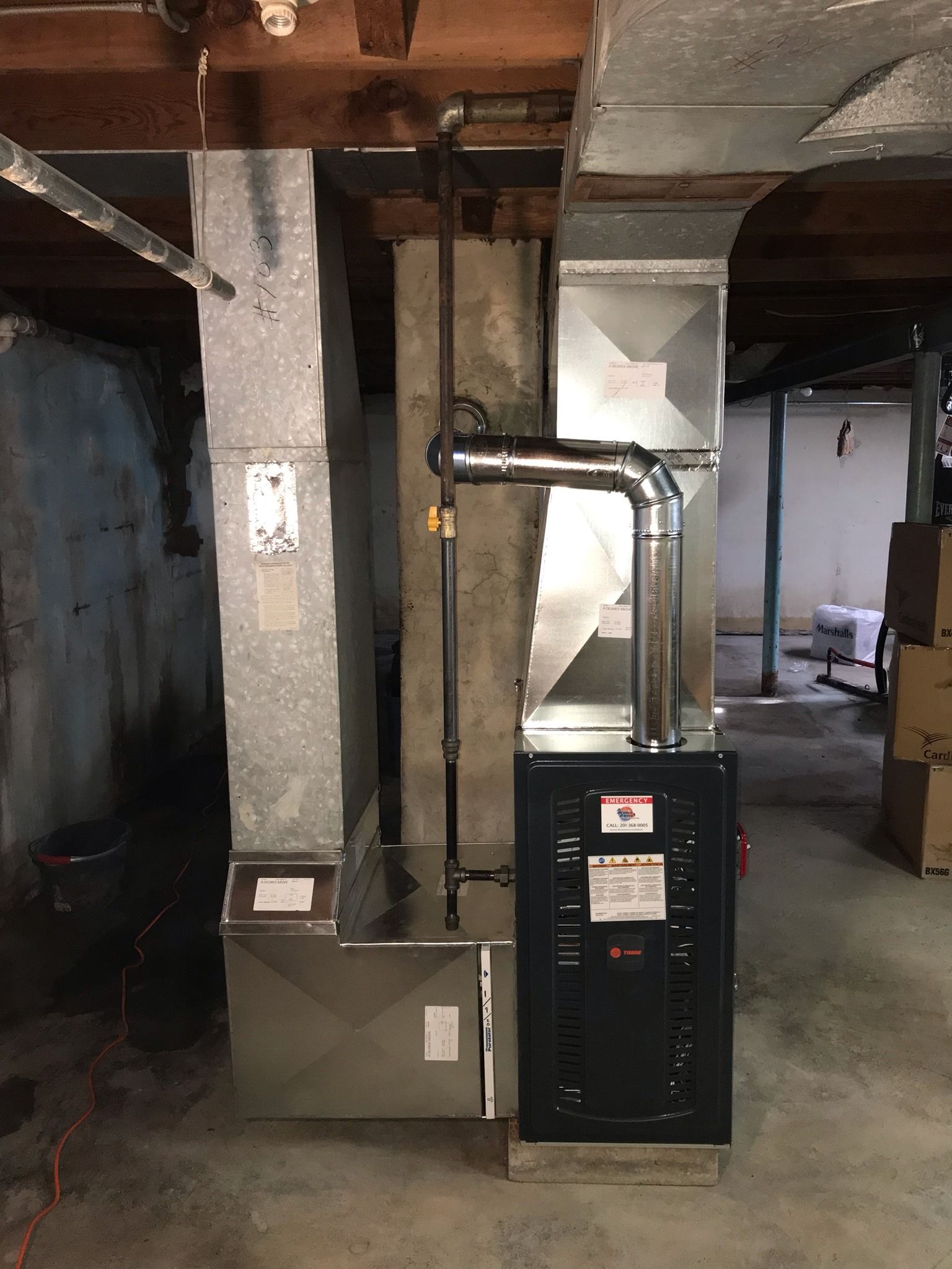 Furnace and ductwork in a basement. The black furnace is connected to silver ducts and pipes.