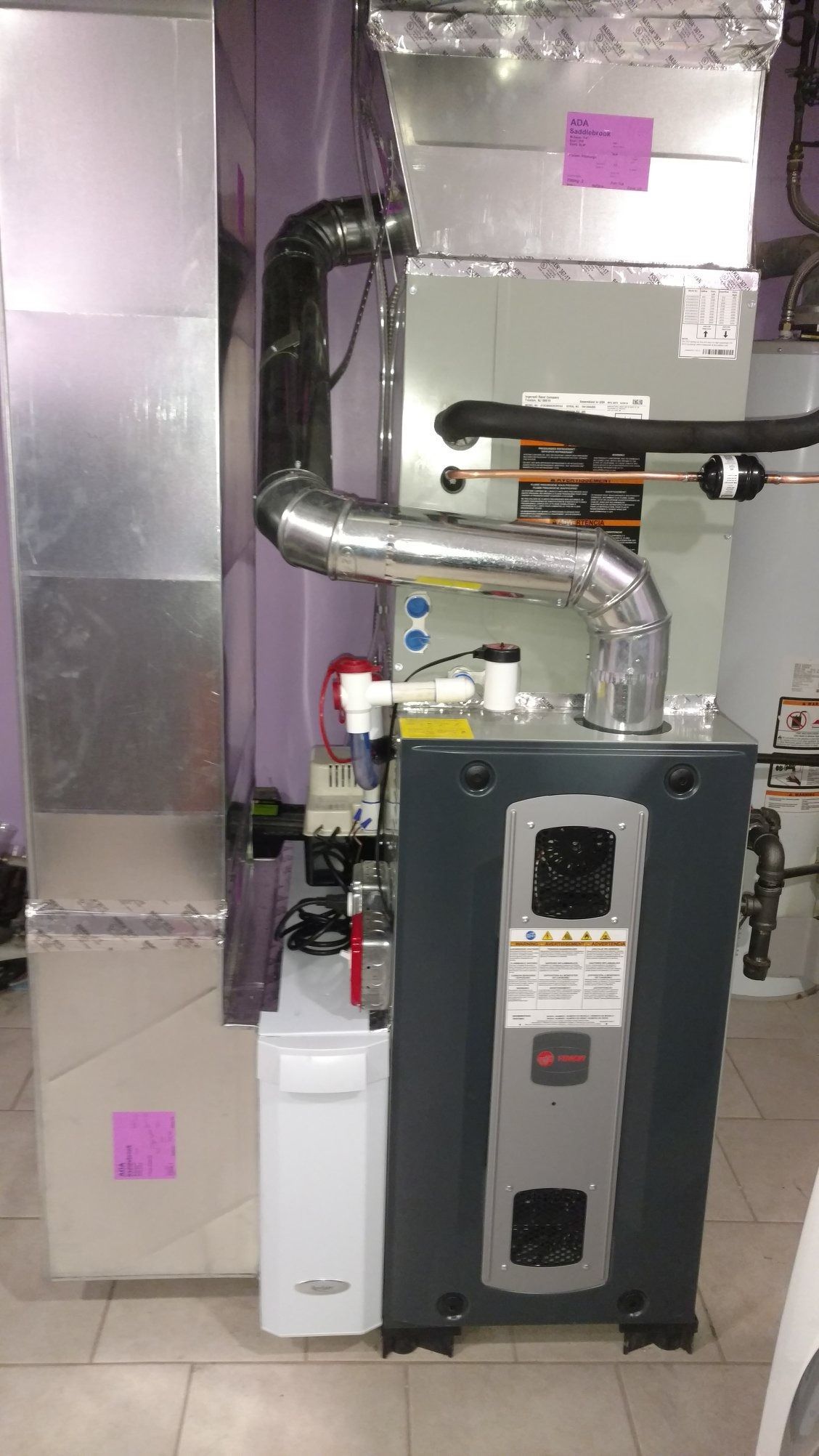 Furnace with ductwork and a condensation pump in a utility room; gray and silver.