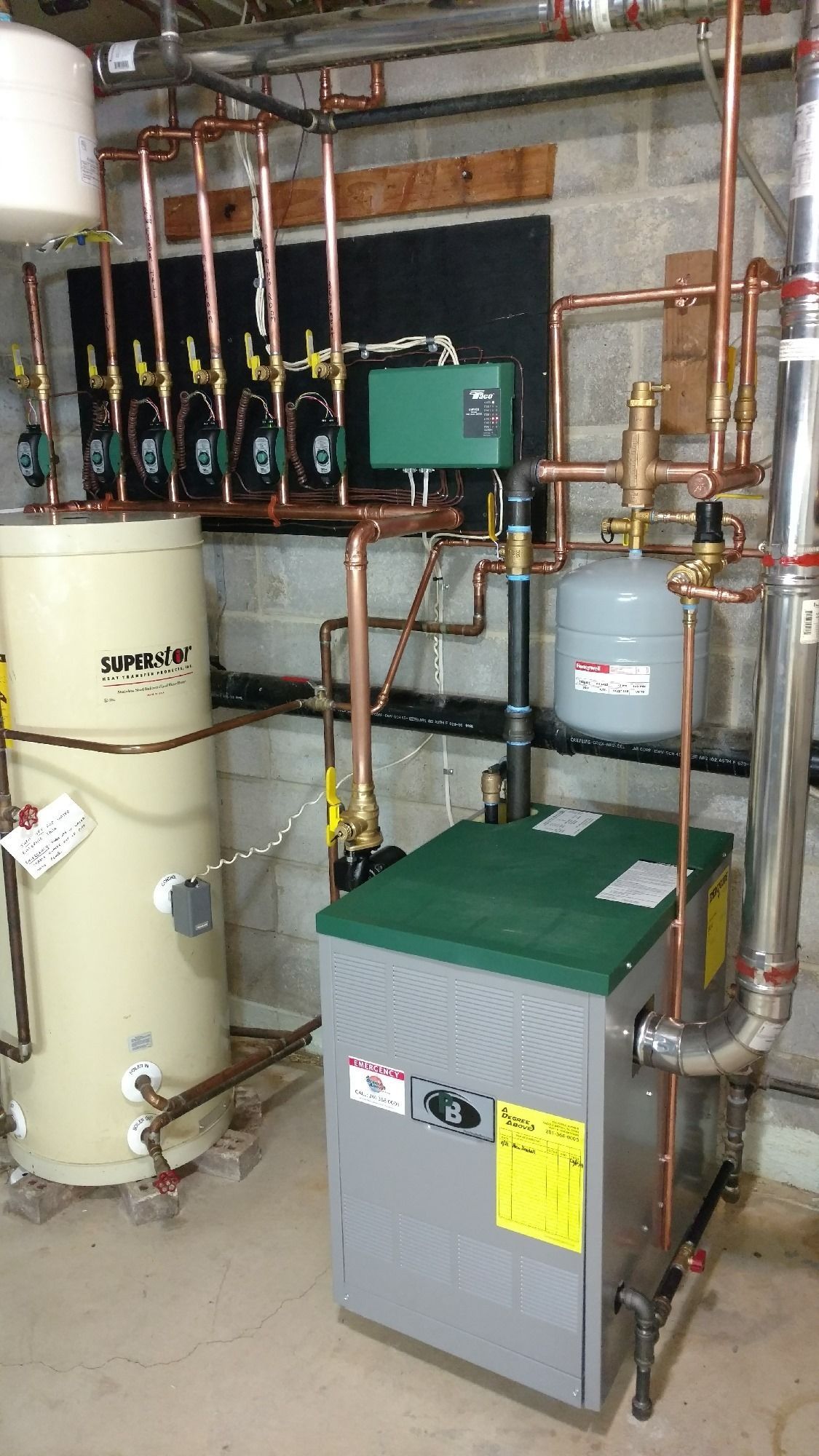 A basement with a residential heating system: boiler, water tank, pipes, and control panel.