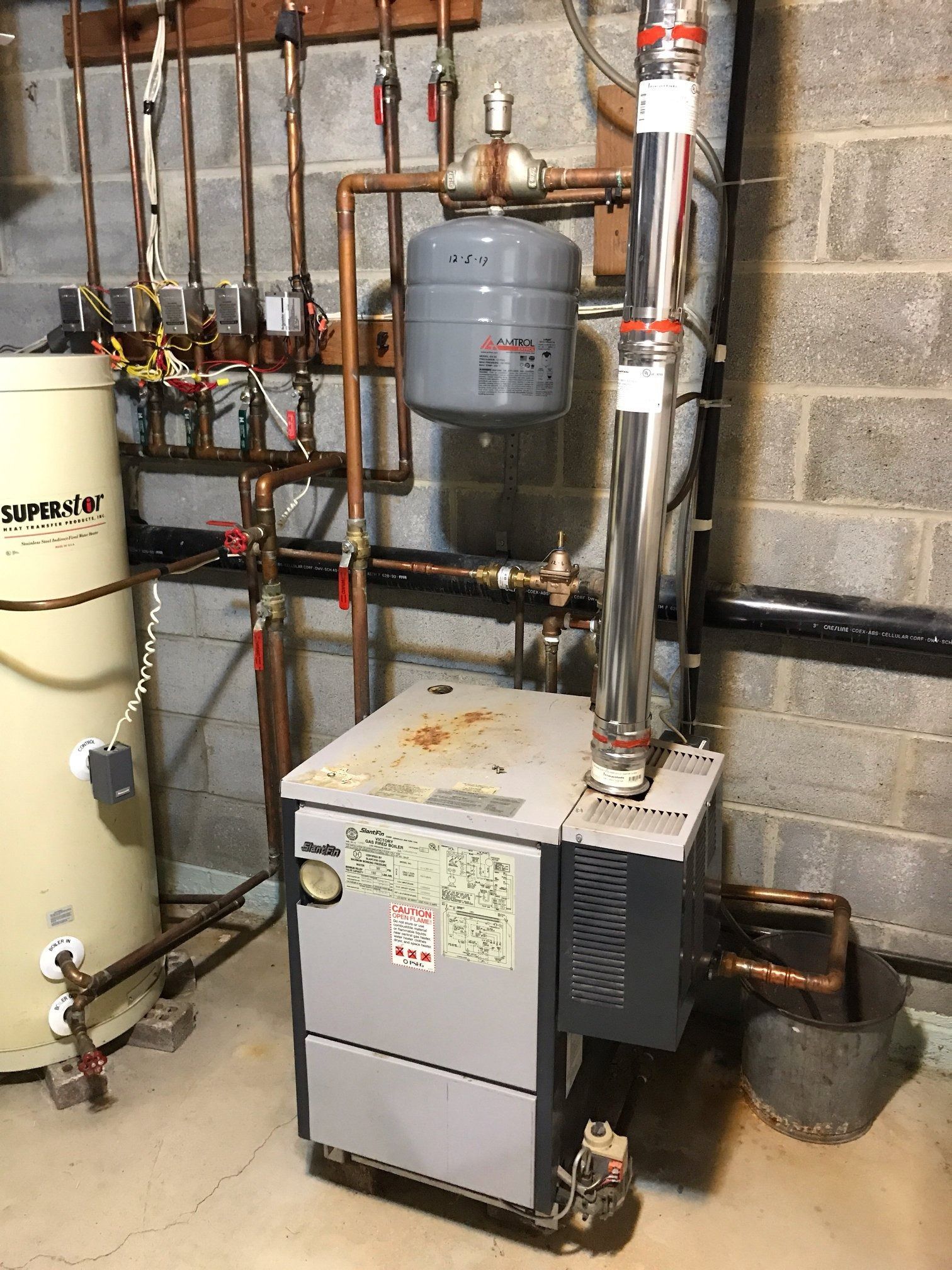 A heating system with pipes, tank, and chimney in a basement setting.