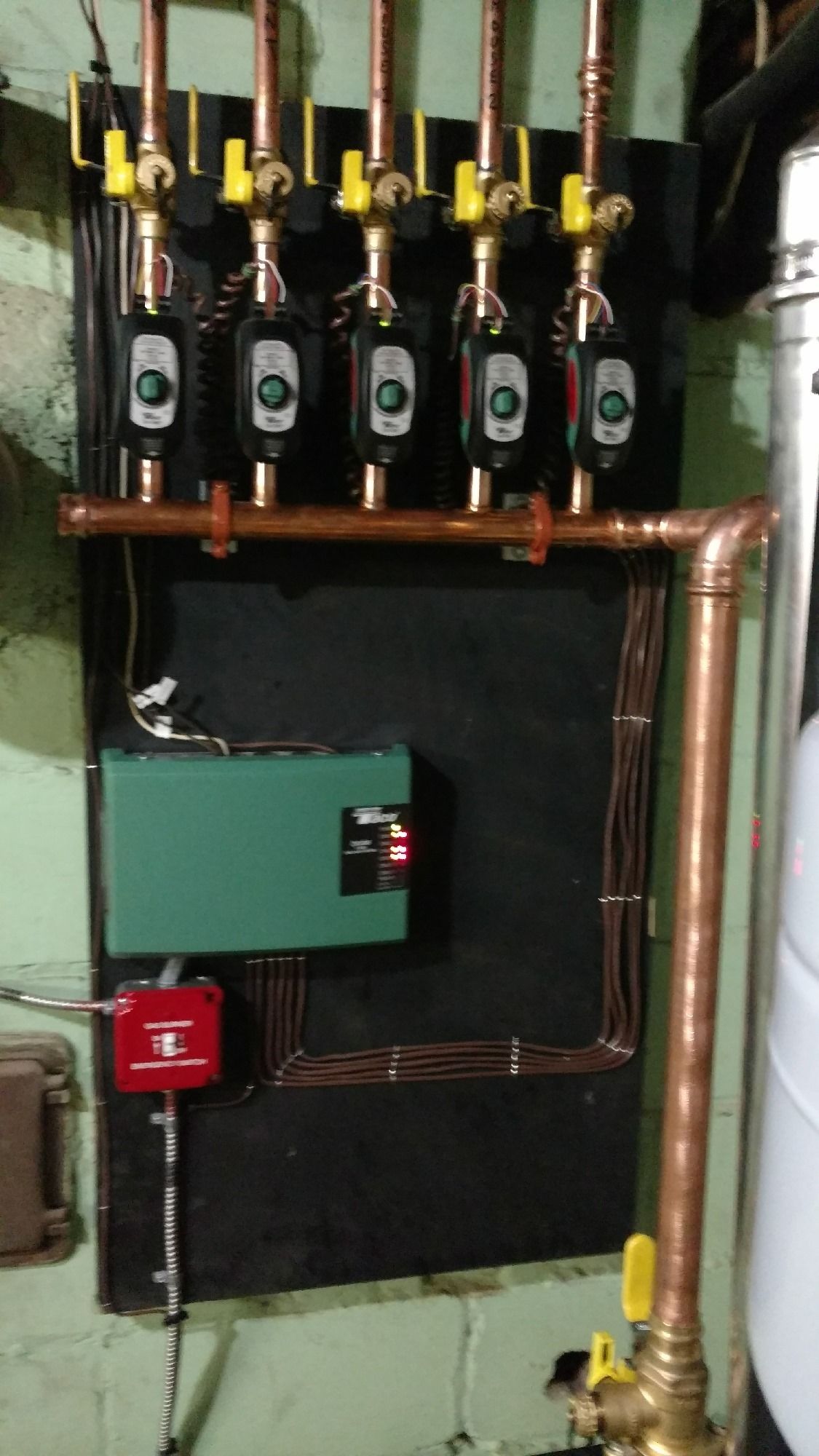 Hydronic heating system with pumps, copper pipes, and a green control panel.