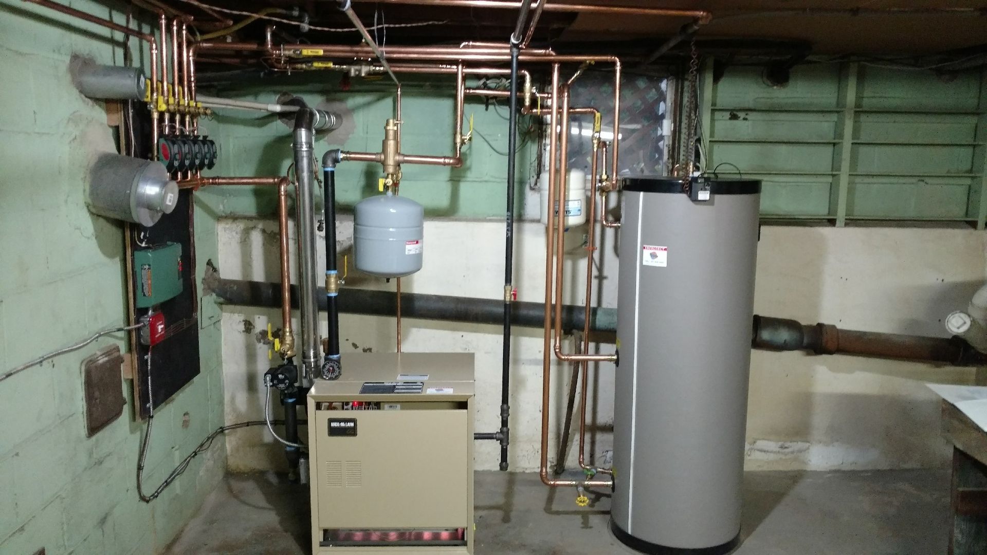 Basement with boiler, water heater, copper pipes, and expansion tank against a concrete wall.