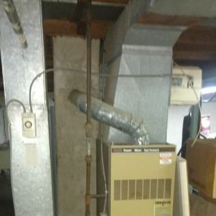 Furnace in a basement, with ductwork and a gas pipe visible.