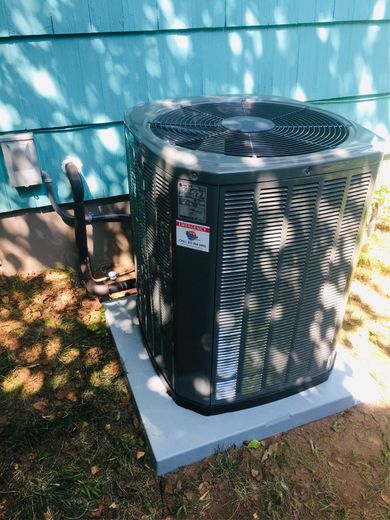 Central air conditioning unit outside a blue house, resting on a gray concrete pad.