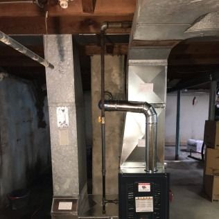 Furnace and ductwork in basement; silver metal, gray concrete walls, wooden beams overhead.
