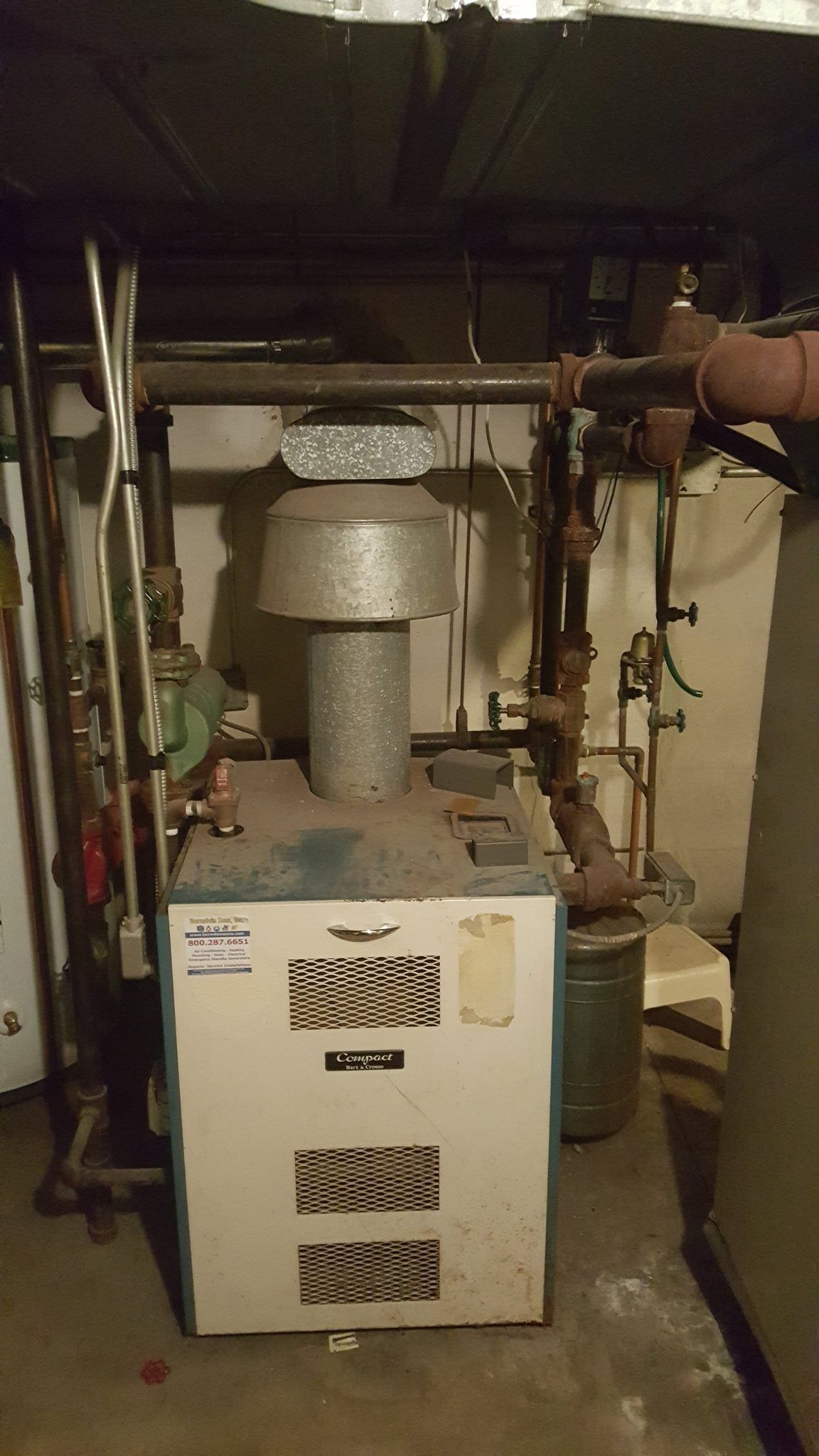 An old, blue furnace with a cylindrical chimney in a dimly lit basement.