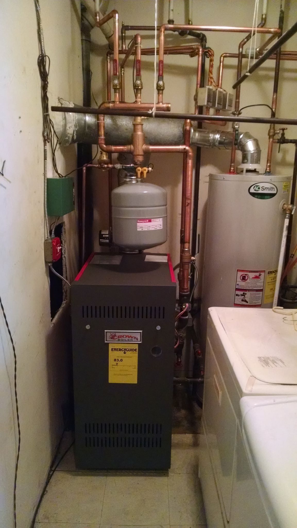 A boiler and water heater with copper piping, expansion tank, and a washing machine in a basement.