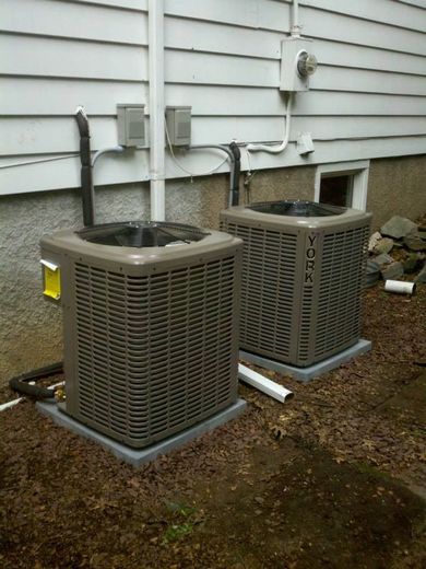 Two York air conditioning units on concrete pads near a house.