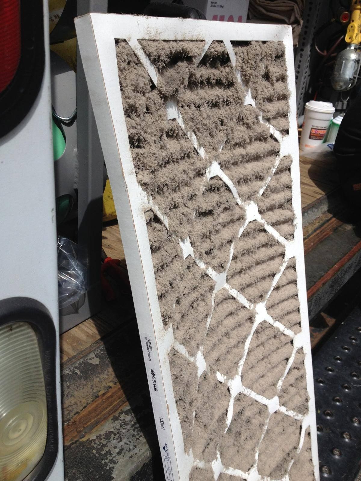 Dirty air filter, covered in dust and debris, against a white frame.