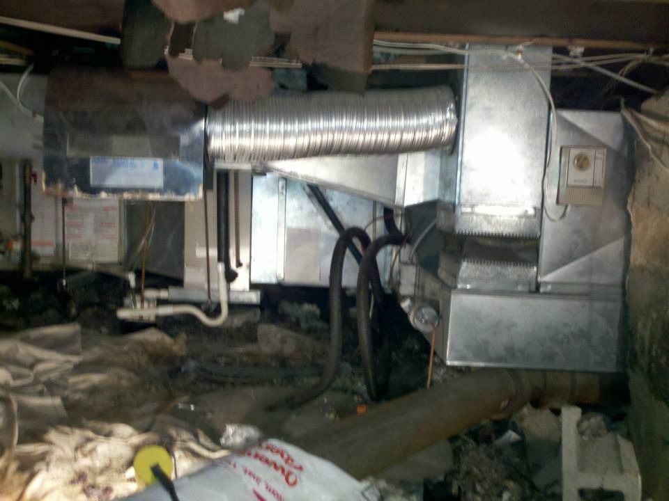 Furnace and ductwork in a crawl space, with flexible silver ducting, and electrical wiring.